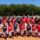 A group photo of softball players in red and blue uniforms on a field.